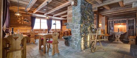 A rustic wooden interior with stone walls, wooden tables, and chairs.