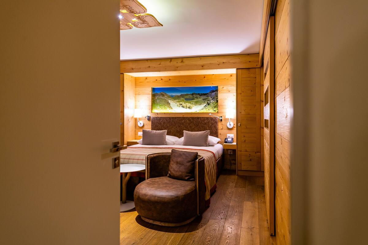 Un dormitorio acogedor con cabecera de madera, cama con almohadas, mesita de noche y una silla.