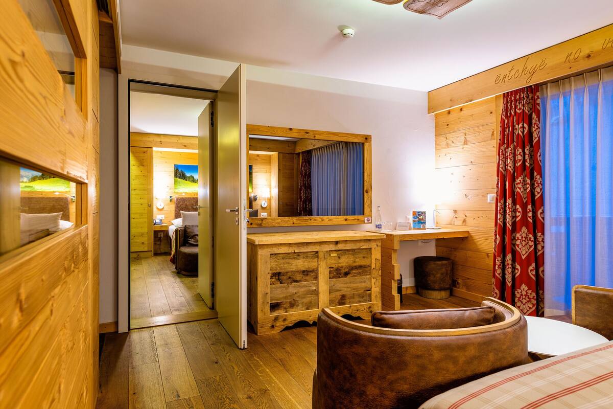Un interior de madera con una cama, un escritorio de madera y un baño visible a través de una puerta abierta.