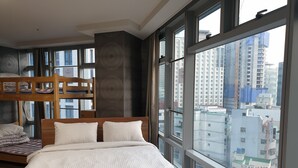 A hotel room with a bunk bed, a large window with a city view, and a bed with white bedding.
