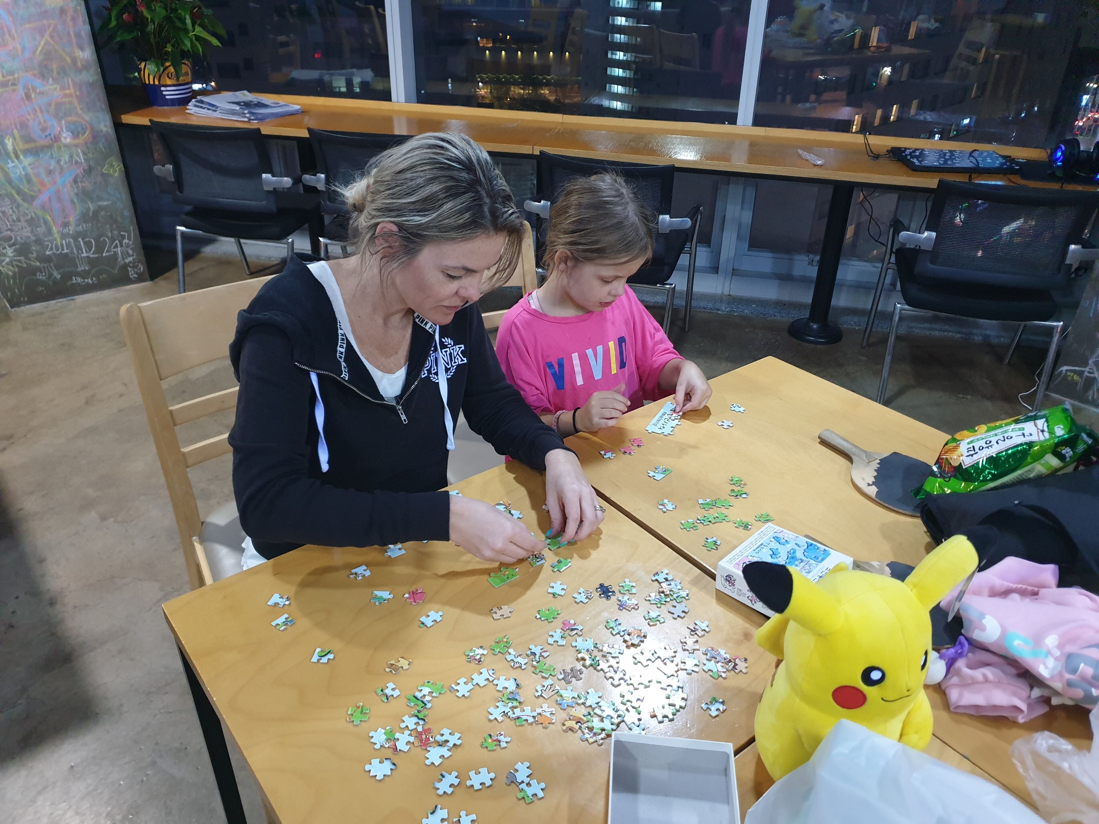 Two people seated at a wooden table with a puzzle in front of them.