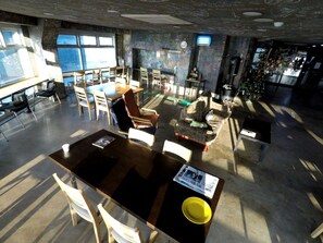 A spacious indoor area with multiple seating options, including tables and chairs, and a couch with a stuffed toy. - Popcorn Hostel Haeundae (Busan)
