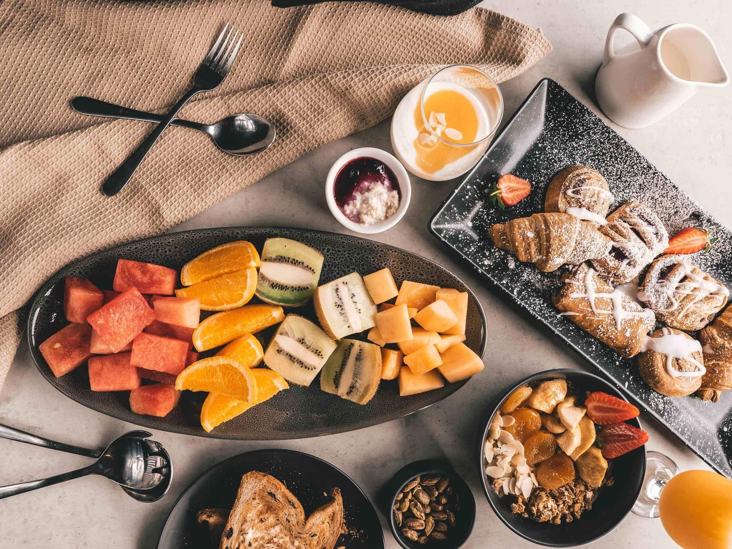A breakfast spread with various fruits, pastries, and a jug of juice.