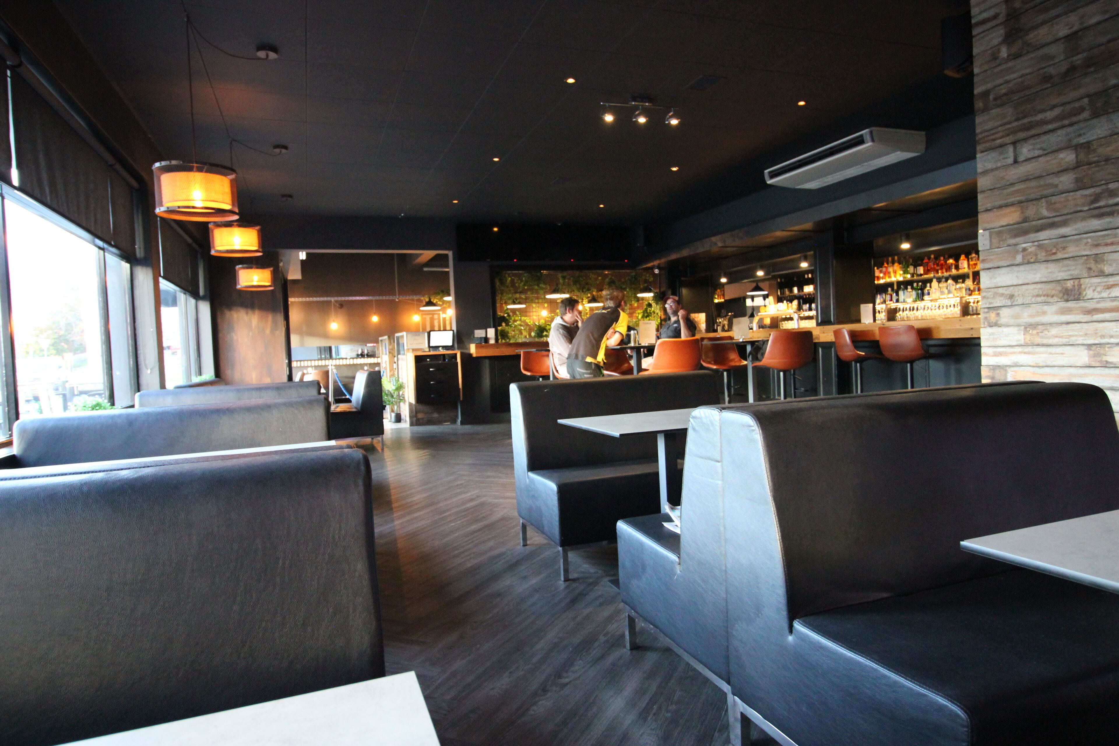 A modern restaurant interior with booth seating, a bar area, and a visible kitchen in the background.