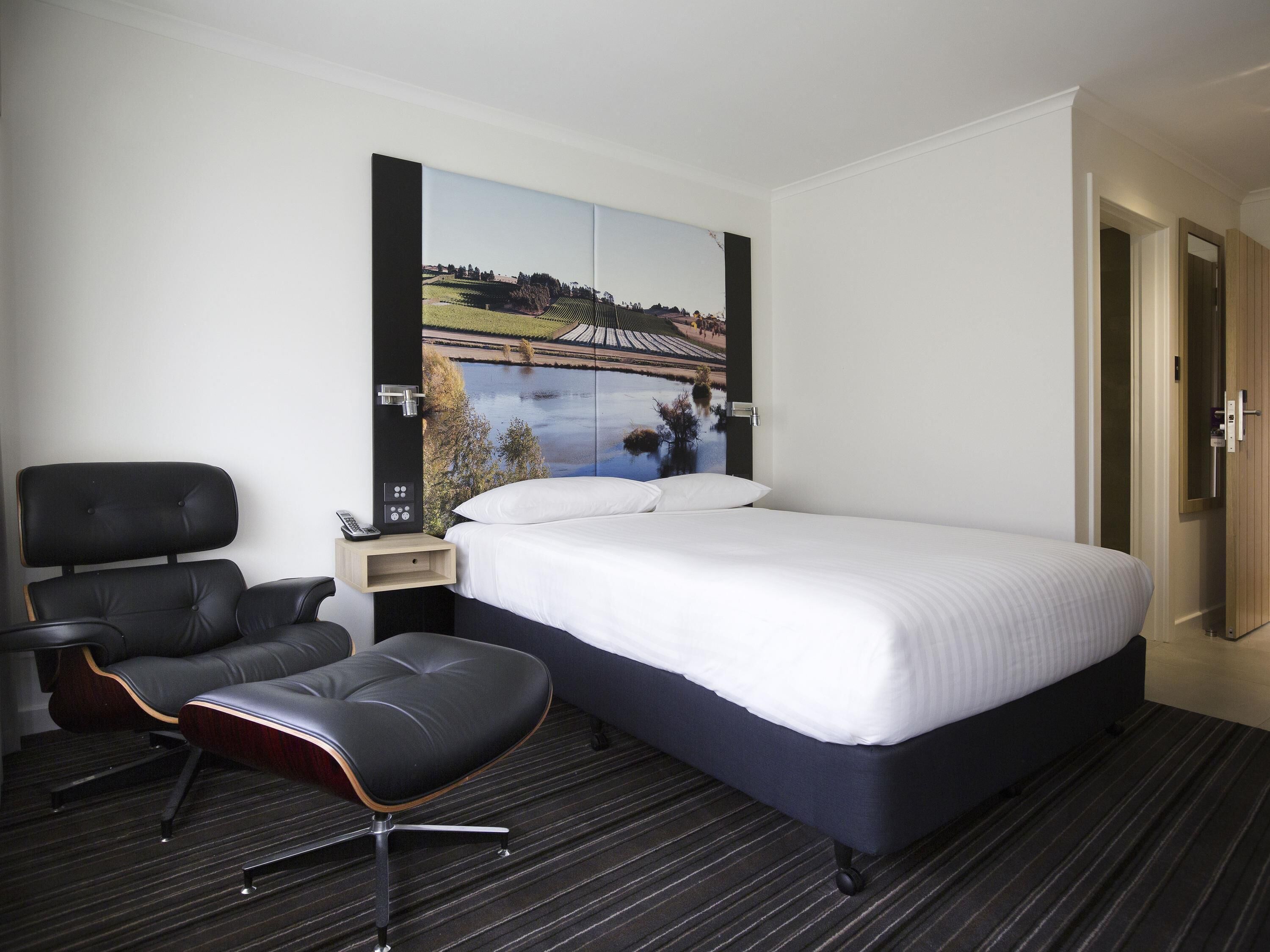 Een hotelkamer met een bed, een stoel, een nachtkastje en een tv aan de muur.