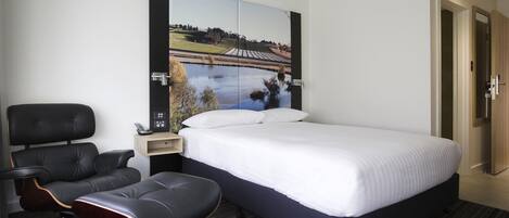 A hotel room with a bed, a chair, a nightstand, and a wall-mounted TV.