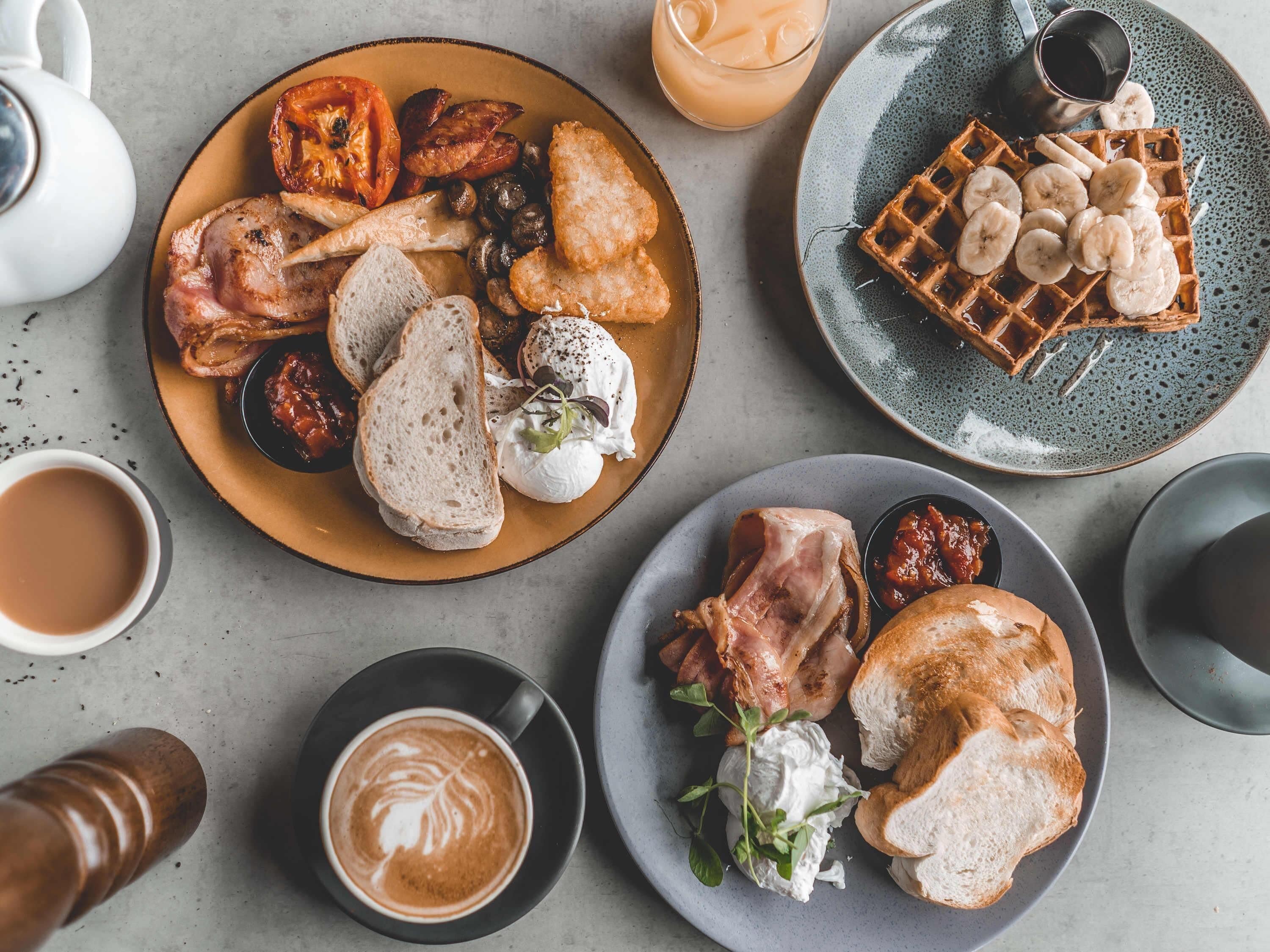 Un desayuno con platos de comida, un waffle, una taza de café y una tetera.