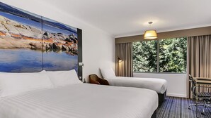 Una habitación de hotel con una cama grande, un escritorio, una silla, una ventana con cortinas y un cuadro en la pared.