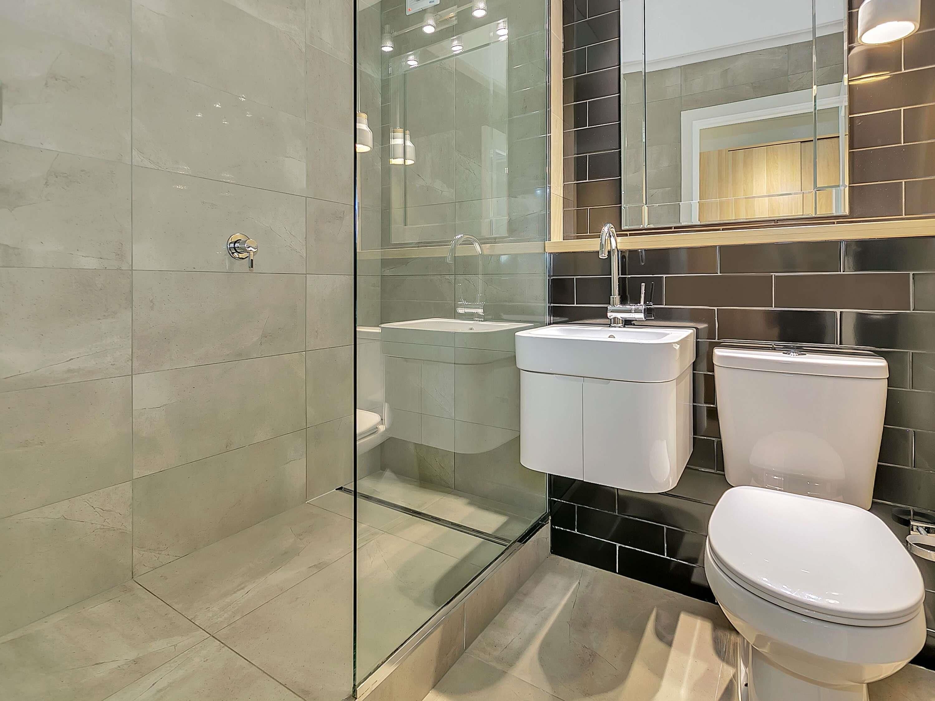 Un baño moderno con cabina de ducha de vidrio, lavamanos doble y retrete.