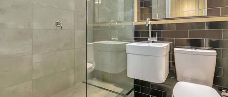 Un baño moderno con cabina de ducha de vidrio, lavamanos doble y retrete.