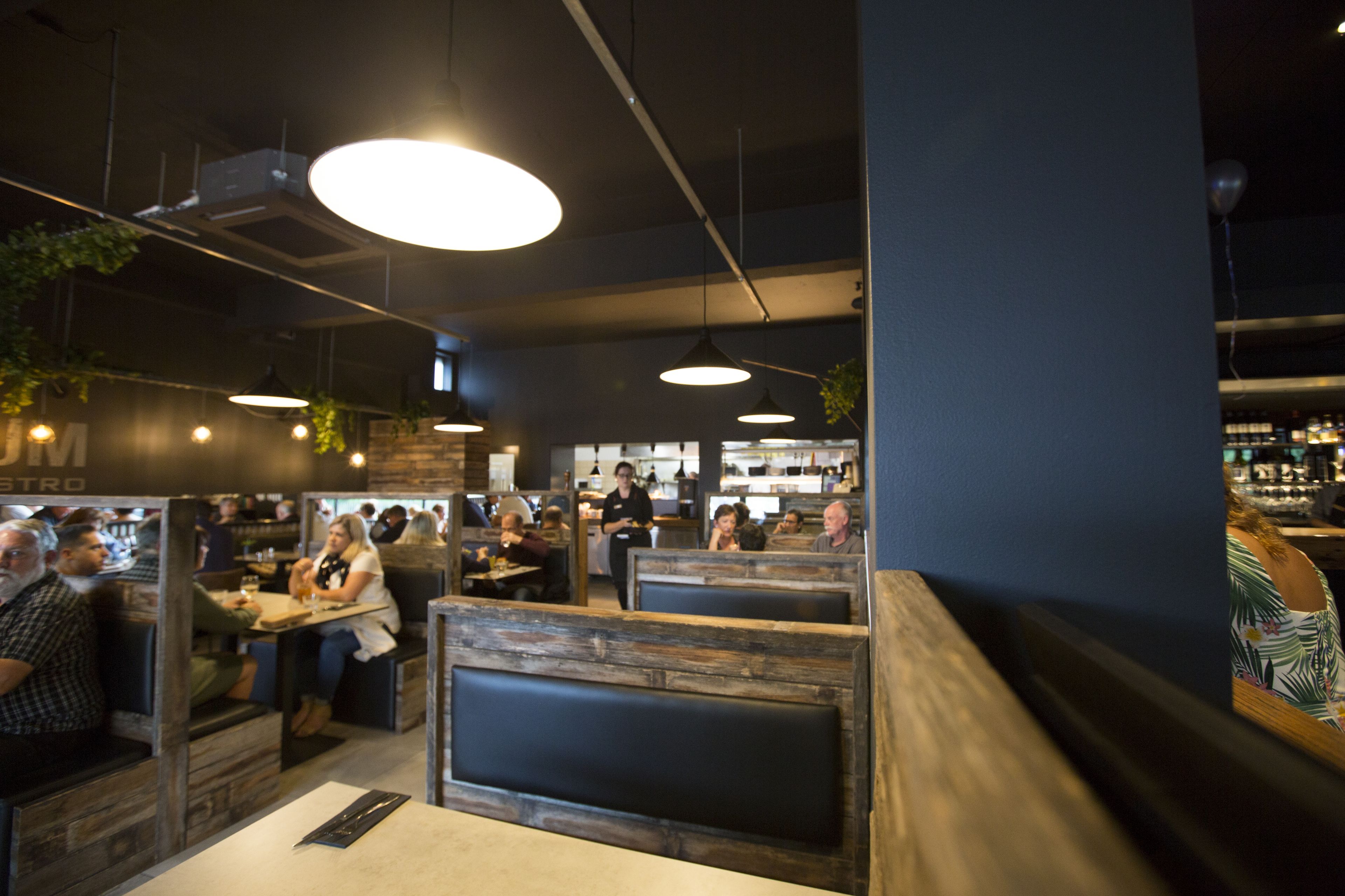 A restaurant with booths and tables, wooden accents, hanging lights, and a bar area.