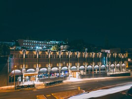 A hotel with a row of covered outdoor seating areas, a visible restaurant, and a large building in the background.