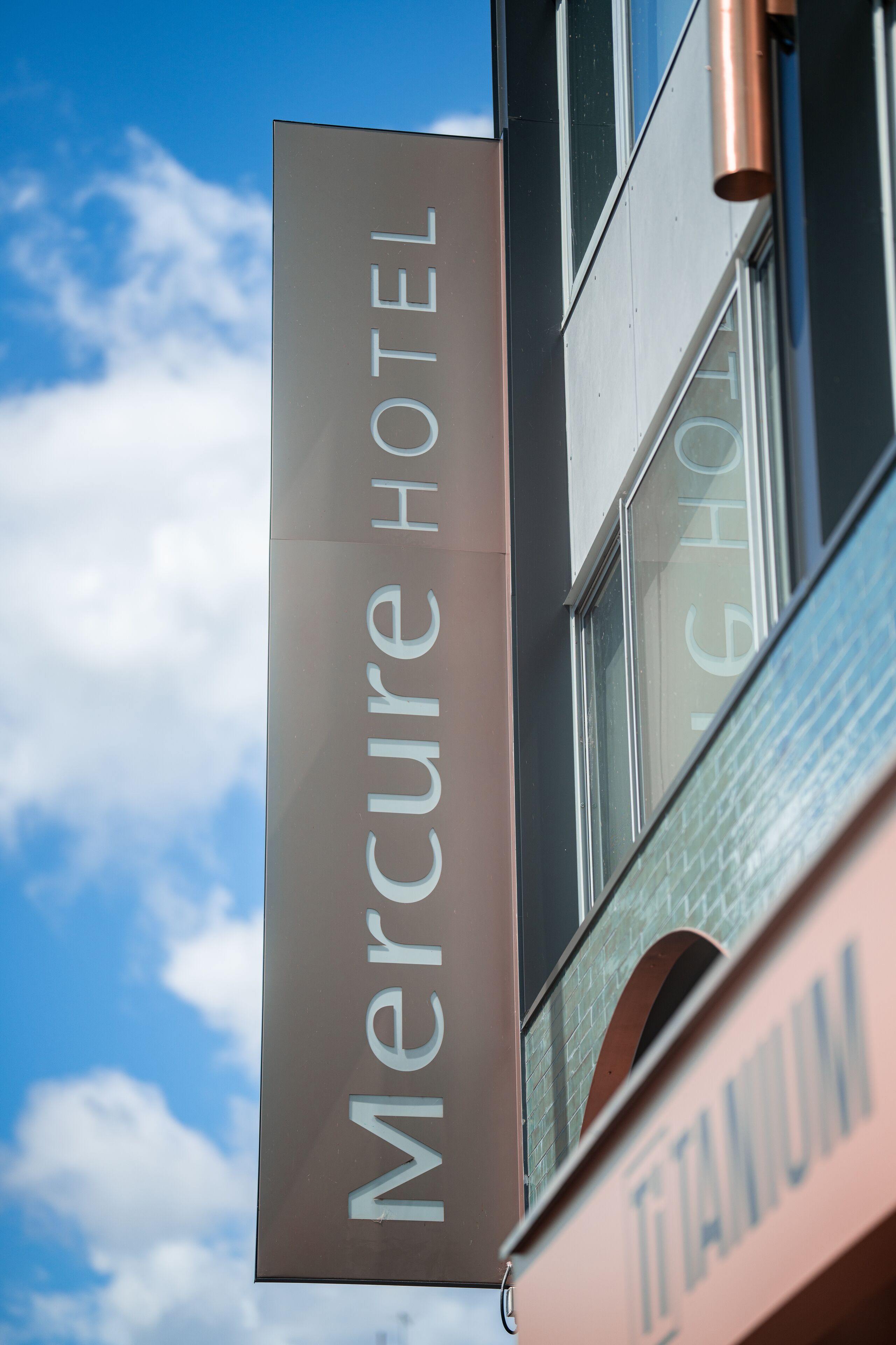 A Mercure Hotel sign with a clear view of the building's architecture and a blue sky with clouds in the background.