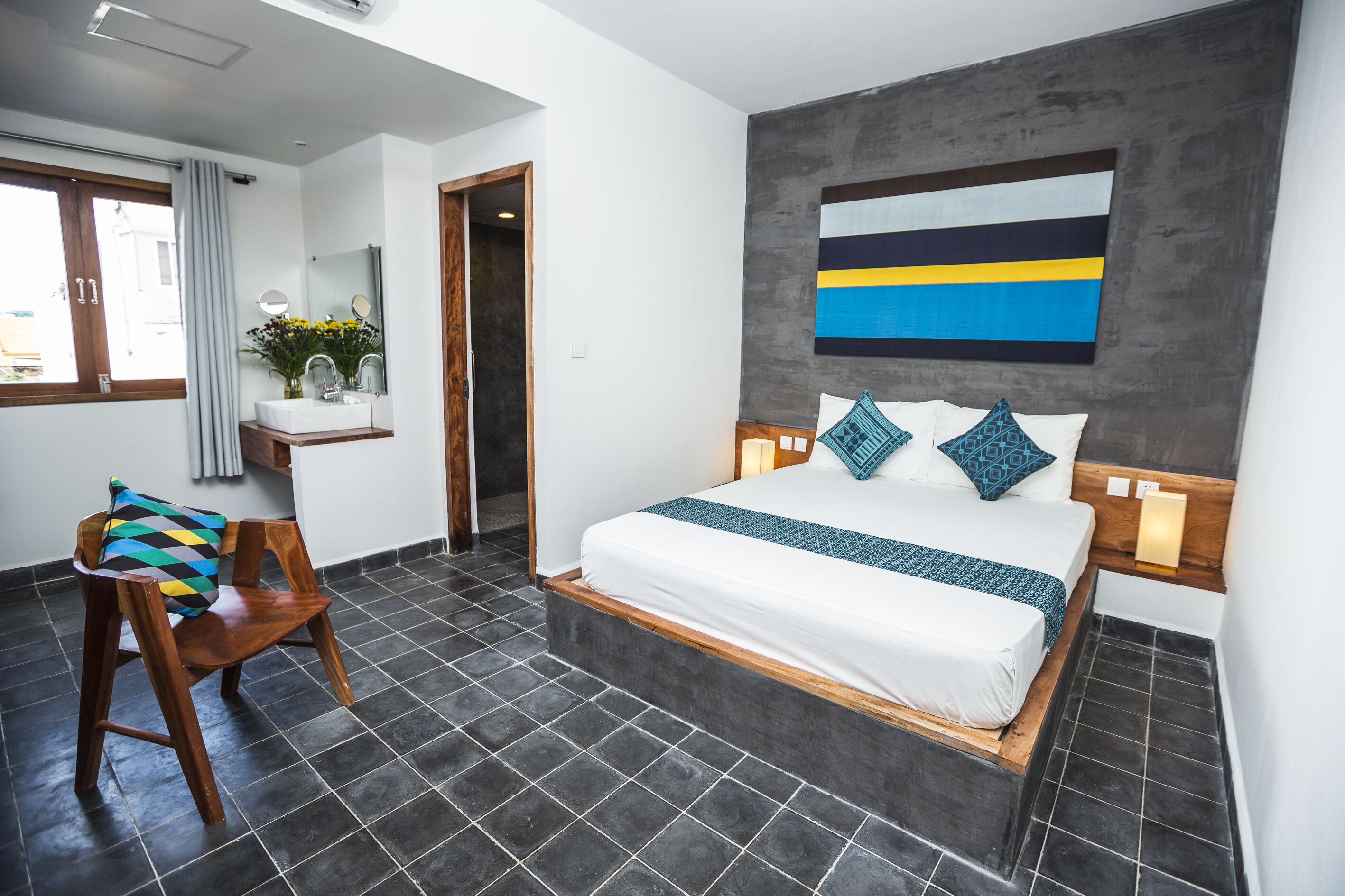 Un dormitorio moderno con una cama grande, una silla de madera, una mesita con un florero y un cuadro en la pared.