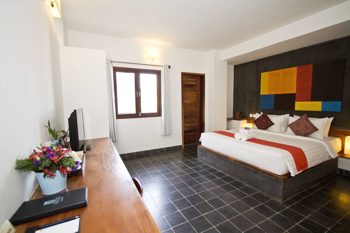 Ein Hotelzimmer mit Bett, Schreibtisch mit Computer, Fenster und Wand mit geometrischem Muster.