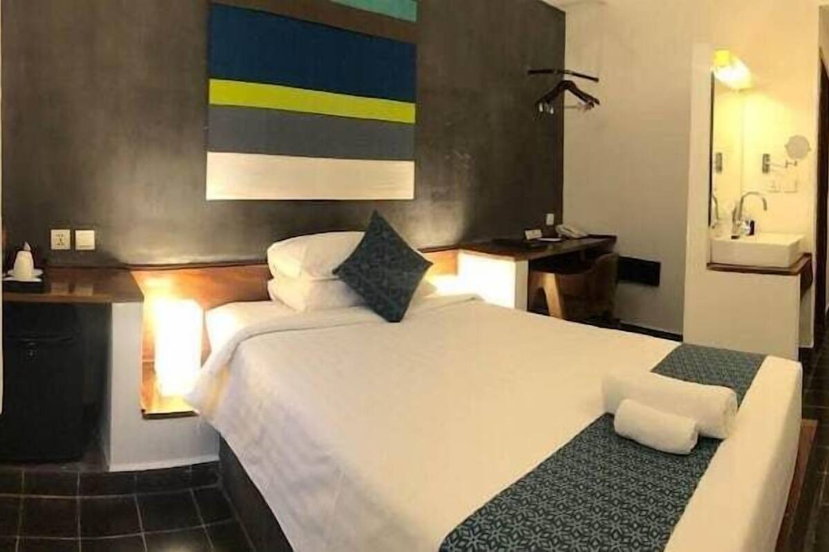 Ein Hotelzimmer mit Bett, Nachttisch, Fernseher und einem Badezimmer mit Spiegel und Waschbecken.