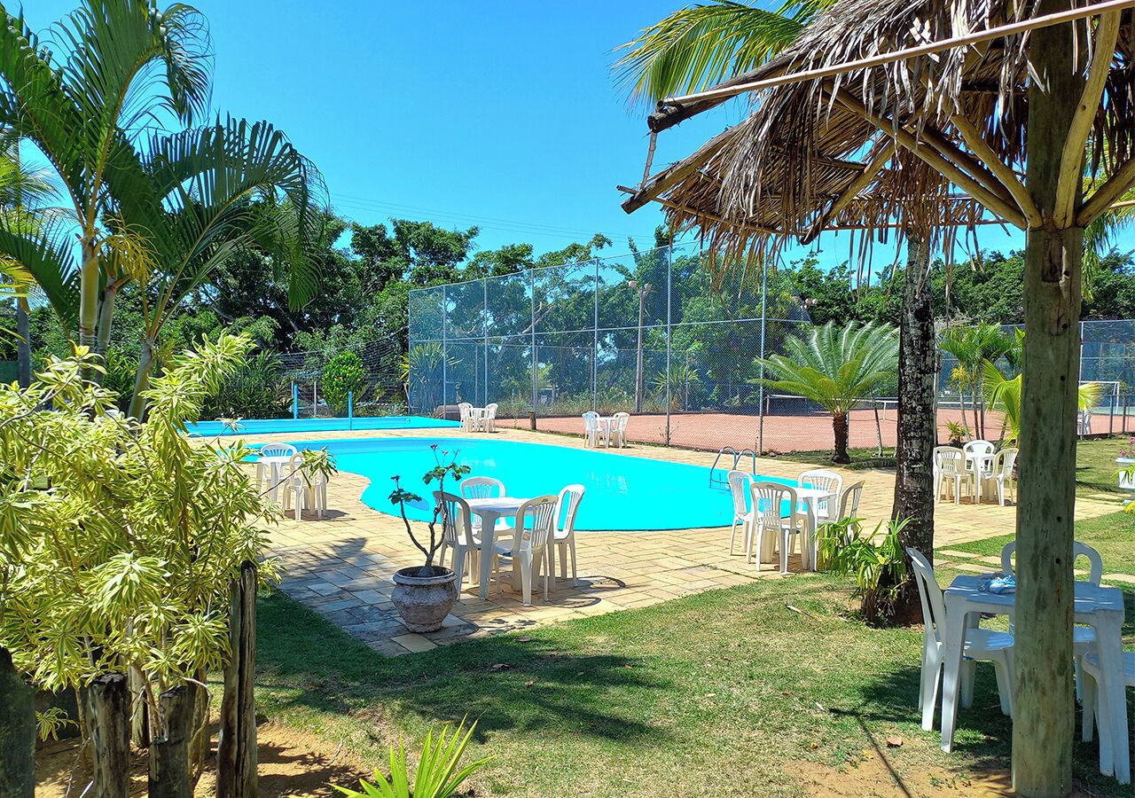 Une piscine entourée de palmiers et d’une clôture, avec des chaises et des tables blanches.