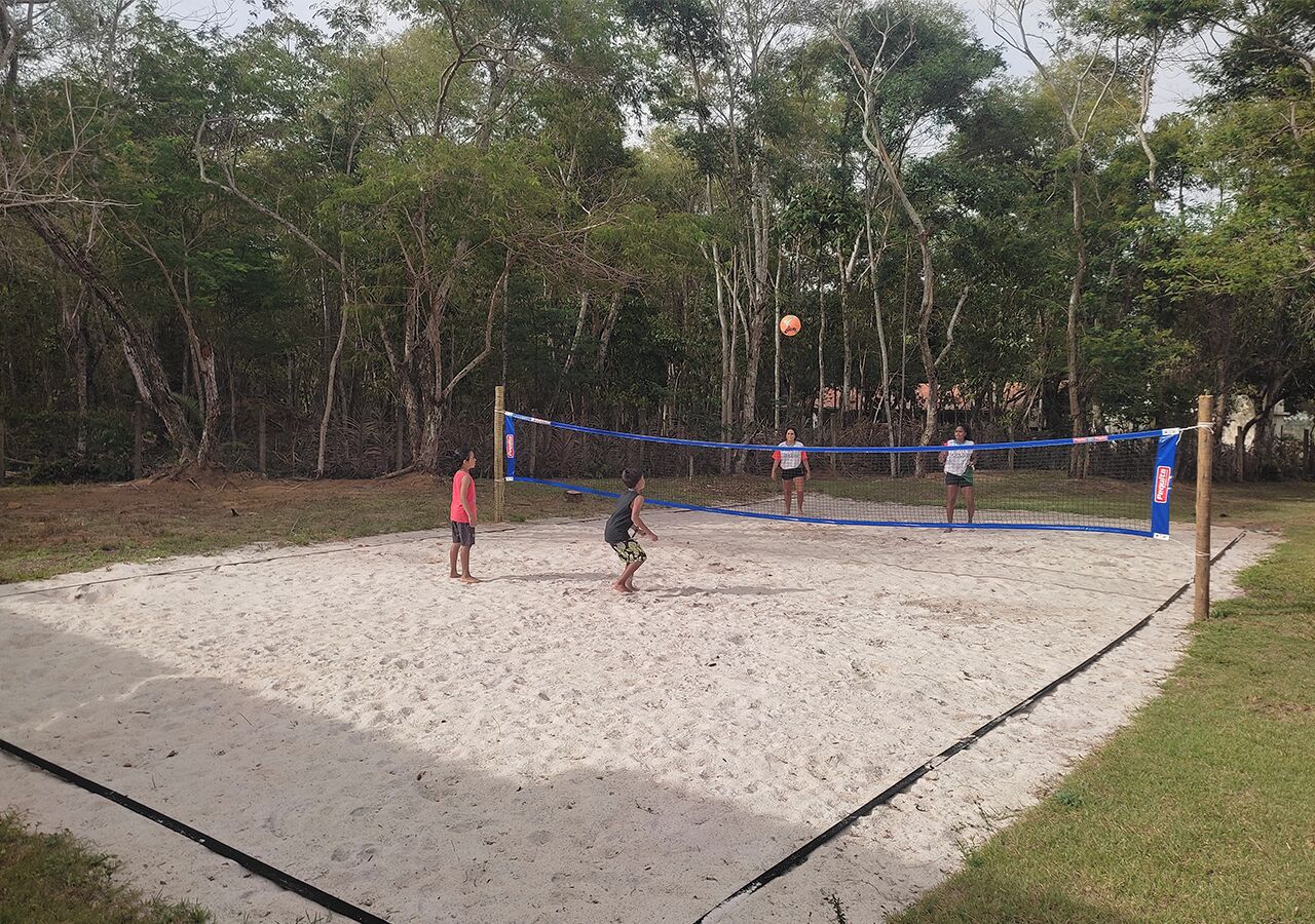 A volleyball game on a sandy court surrounded by trees.