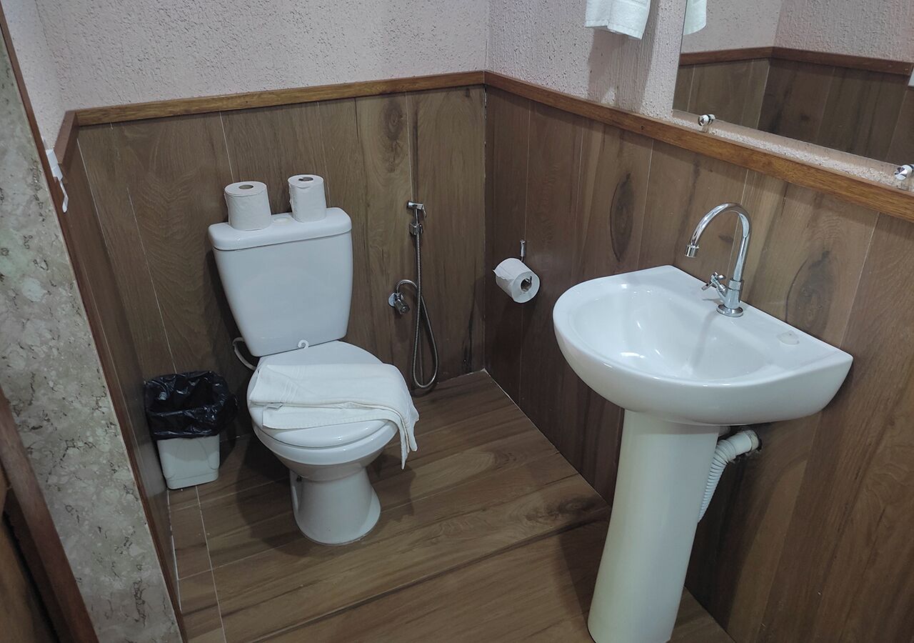 A bathroom with a wooden floor, a white toilet, a white sink, and a wooden wall panel.