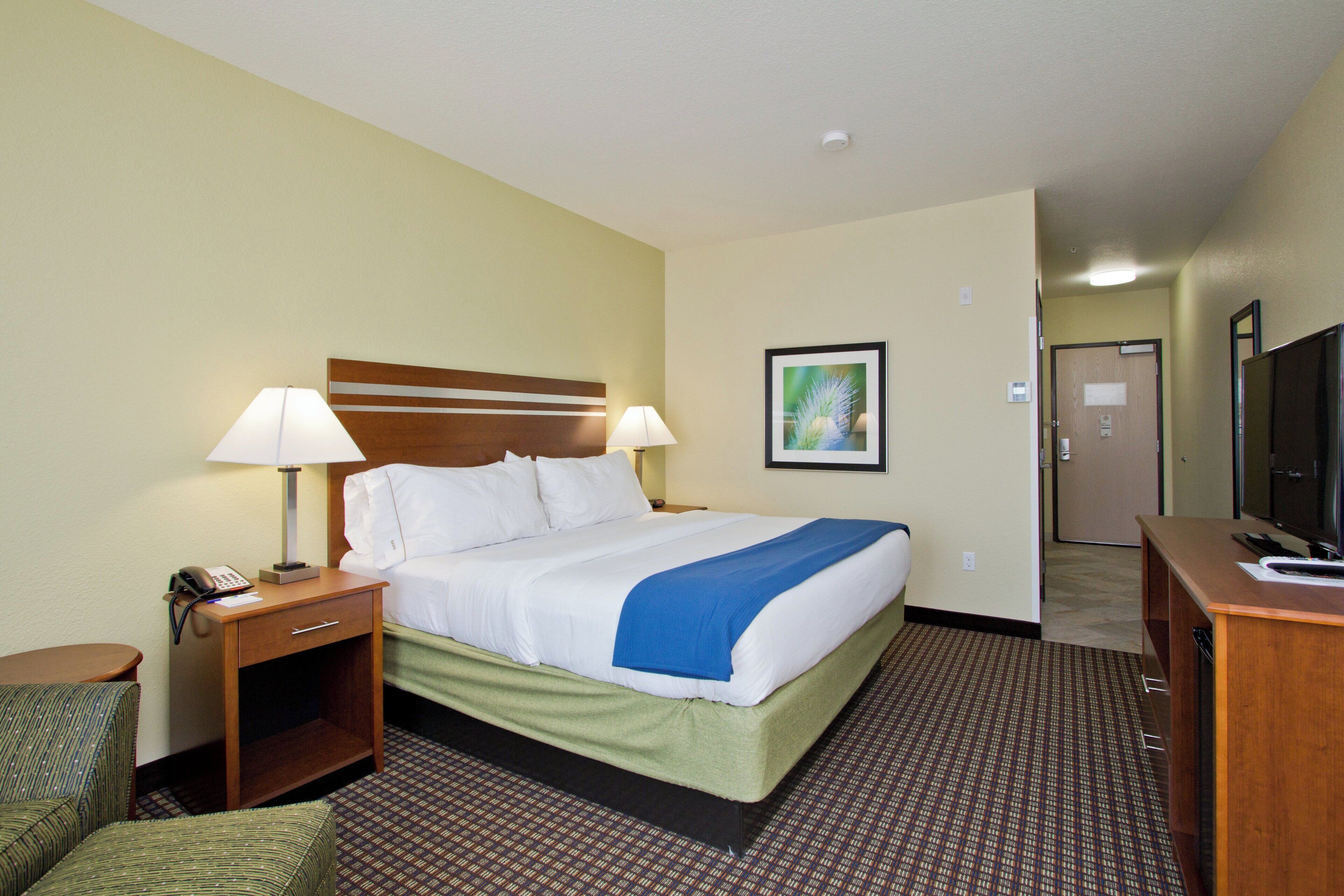 A hotel room with a bed, bedside lamps, a desk with a television, and a chair.