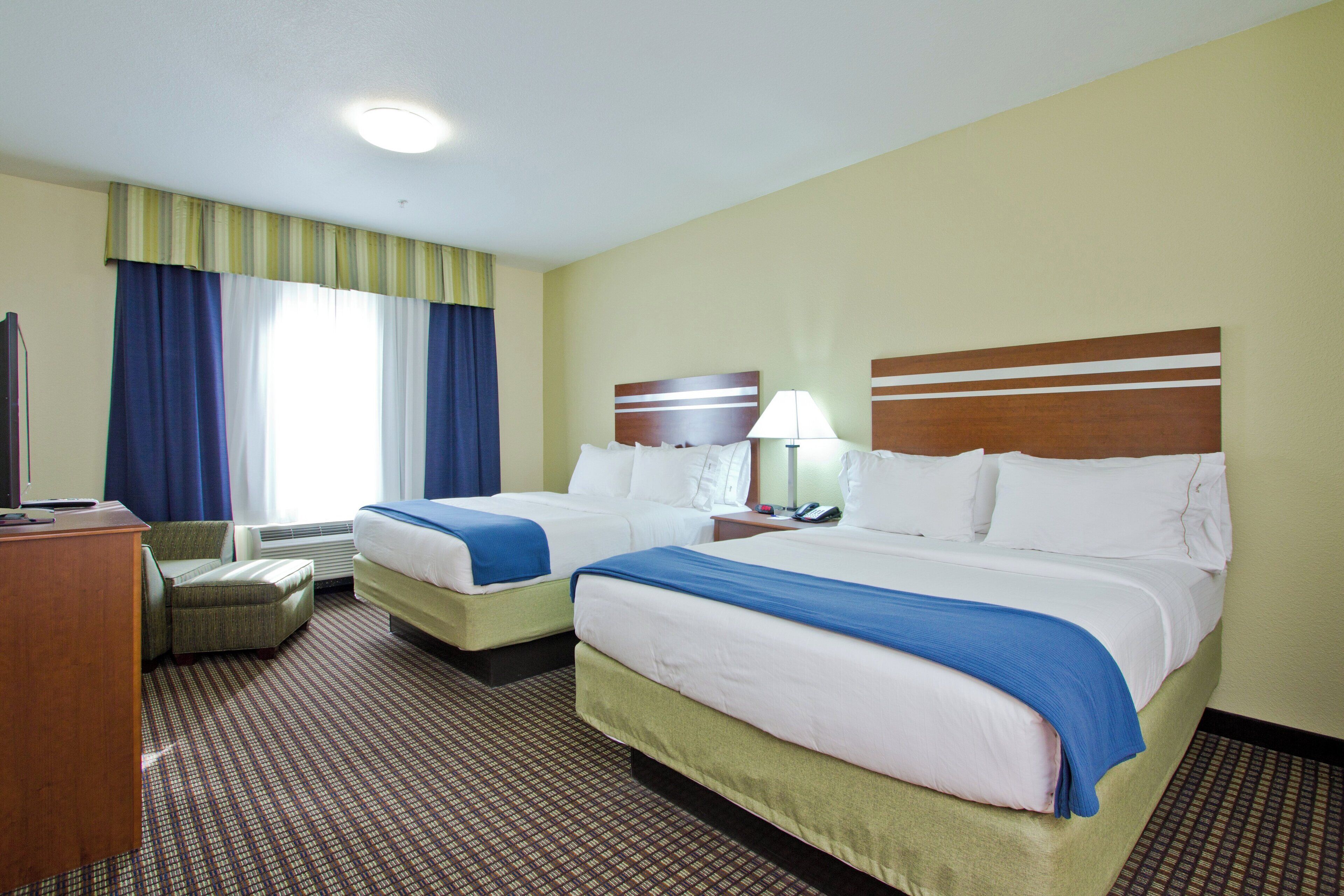 Habitación de hotel con dos camas, un escritorio, una silla y una ventana con cortinas.