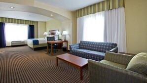 Una habitación de hotel con cama, sofá, mesita y escritorio con lámpara.