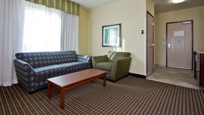 A hotel room with a patterned carpet, a sofa, a chair, a small table, and a door with a sign.