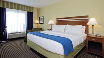 A hotel room with a large bed, two bedside lamps, a chair, a desk, and a window with curtains.