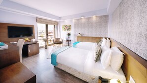Een hotelkamer met twee bedden, een bureau, een stoel, een televisie en een balkon met uitzicht.