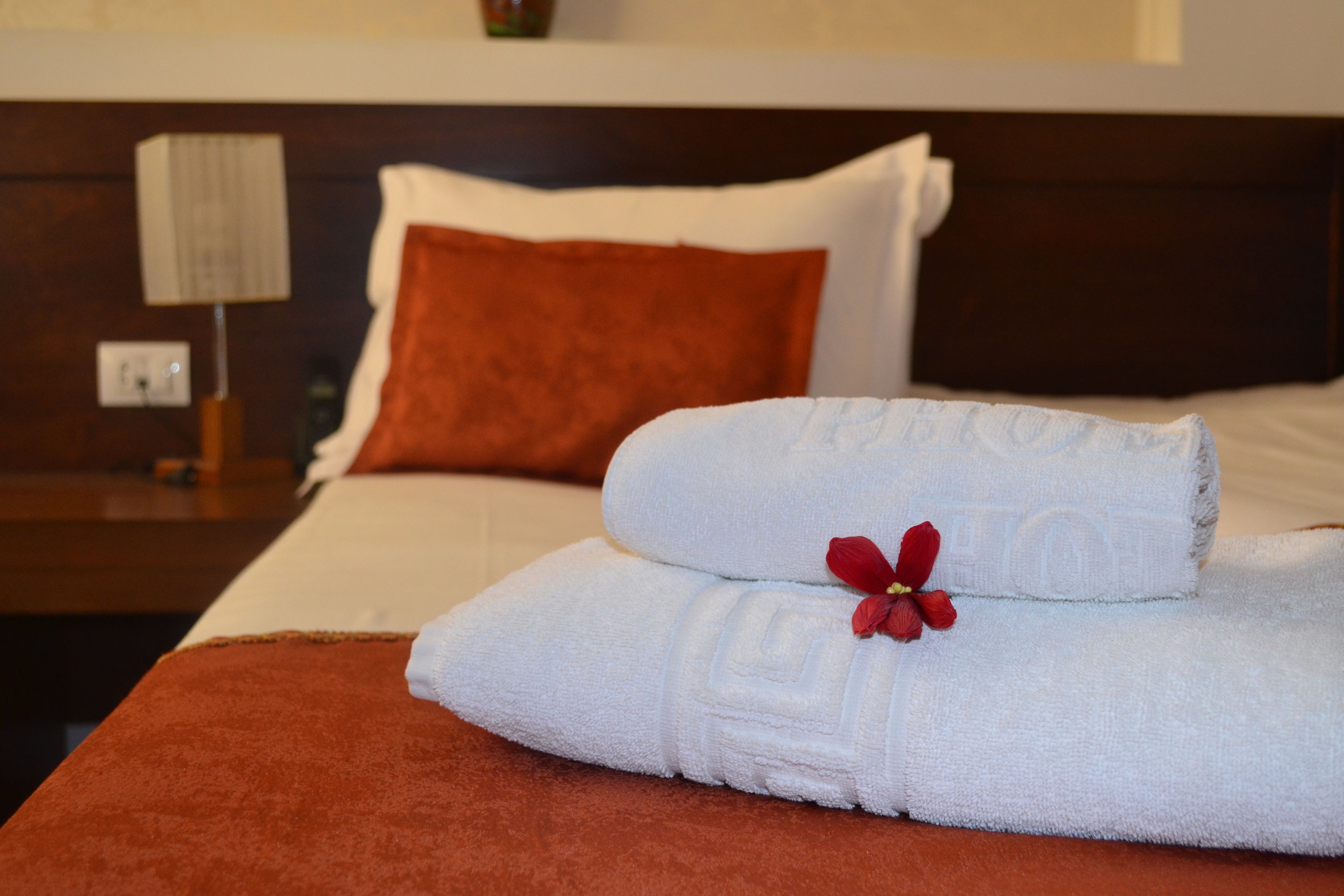 Una cama bien hecha con sábanas blancas, una flor roja, un plaid marrón y un cabecero de madera.