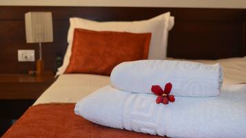 Una cama bien hecha con sábanas blancas, una flor roja, un plaid marrón y un cabecero de madera.