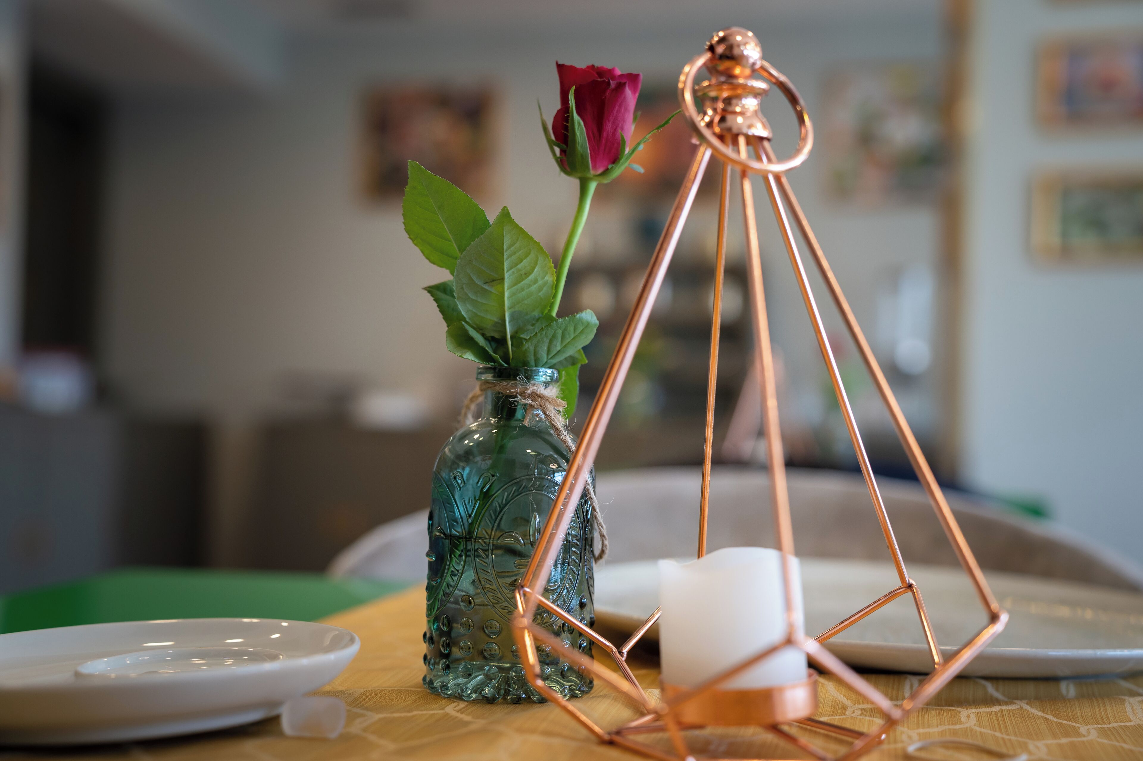 Un tavolo con un vaso di vetro contenente una rosa, una candela e una scultura in metallo geometrica.