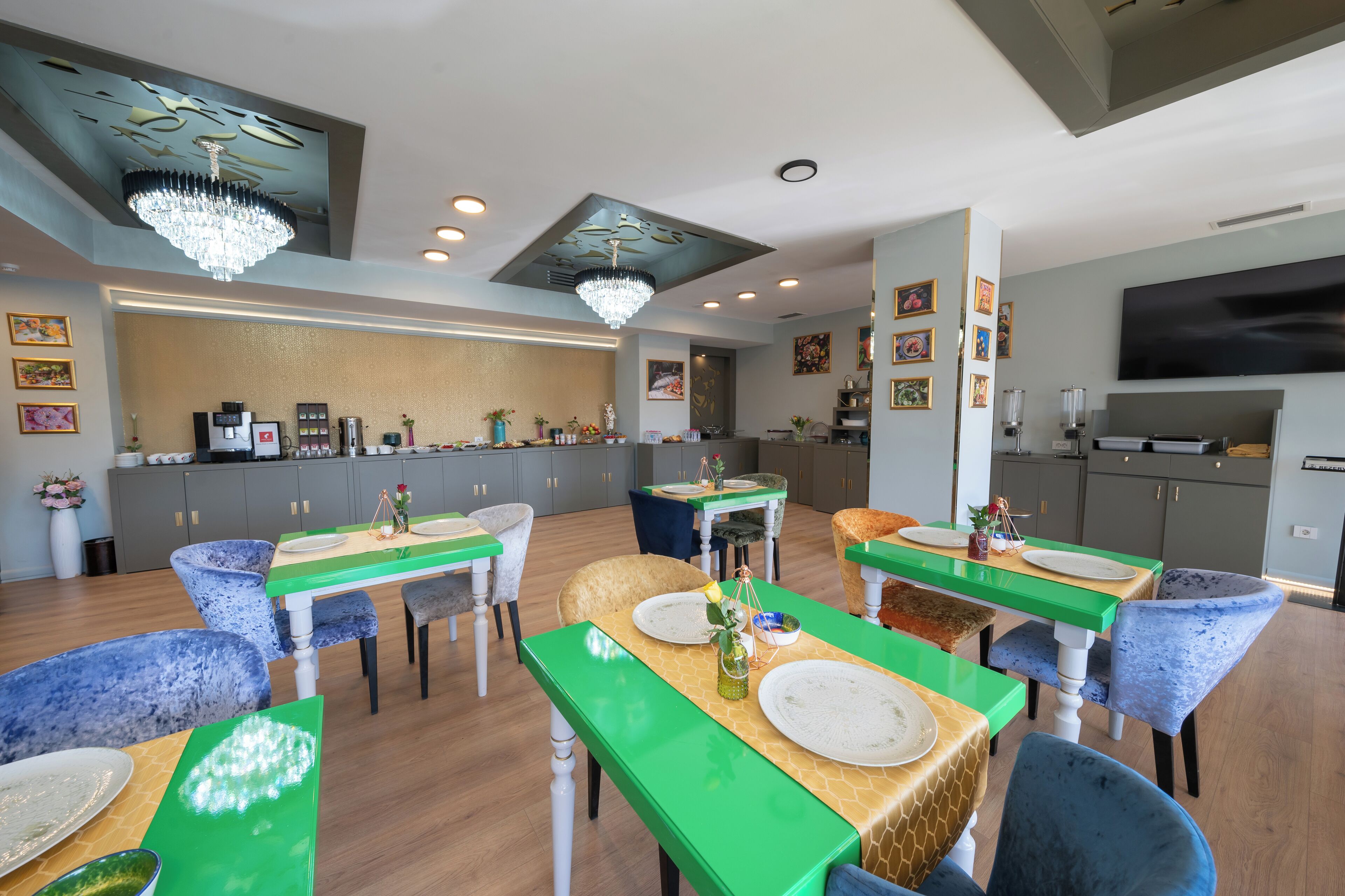 Un comedor moderno con mesas verdes y sillas azules, una araña y una cocina al fondo.