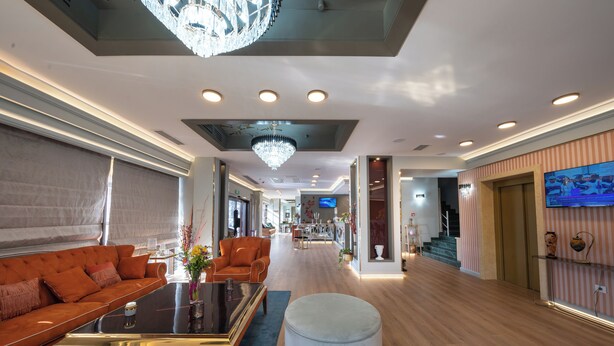 Een moderne hotelentree met een grote bank, een rond poefje, een salontafel en een kroonluchter.