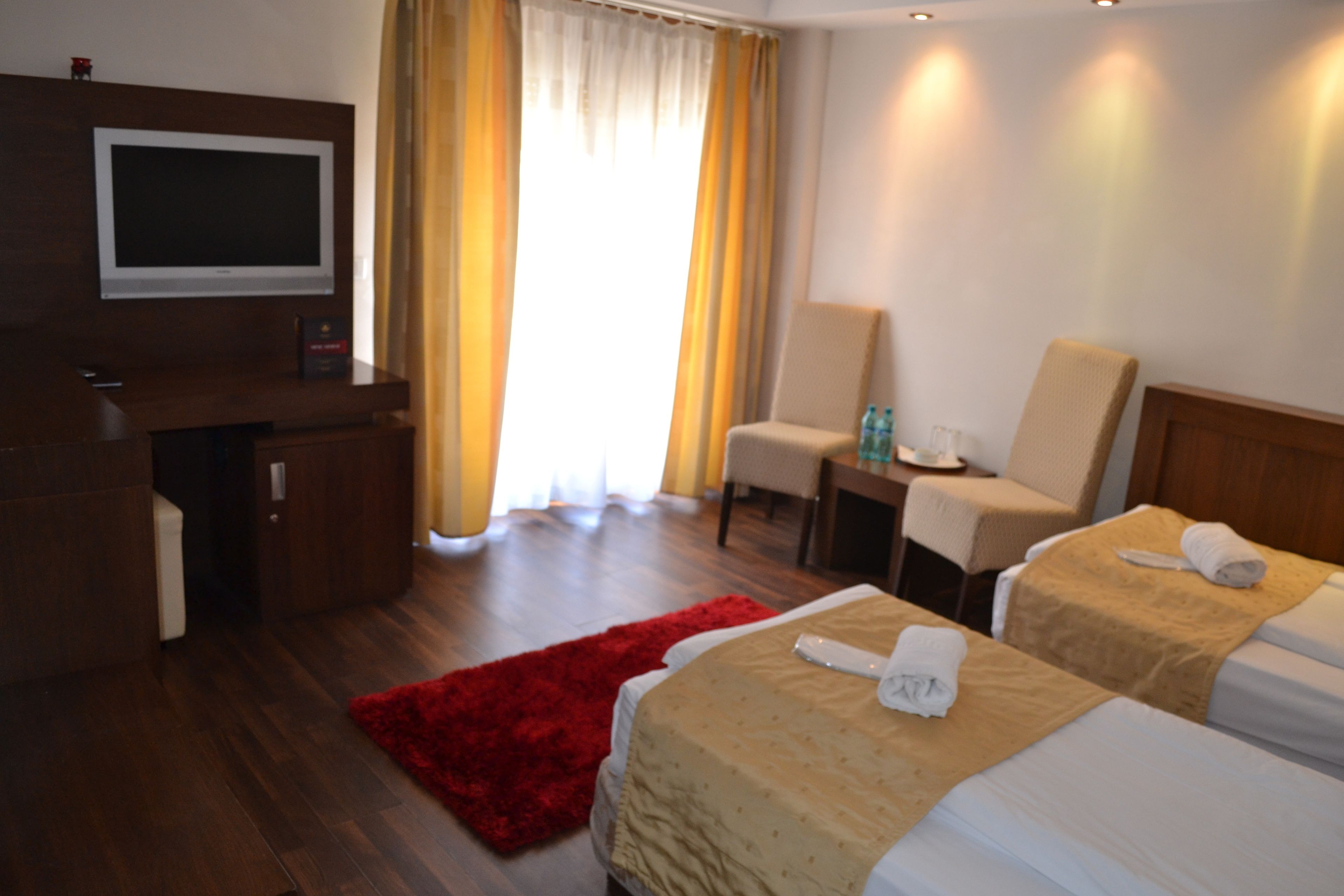 A hotel room with two beds, a desk, a TV, and a red rug.