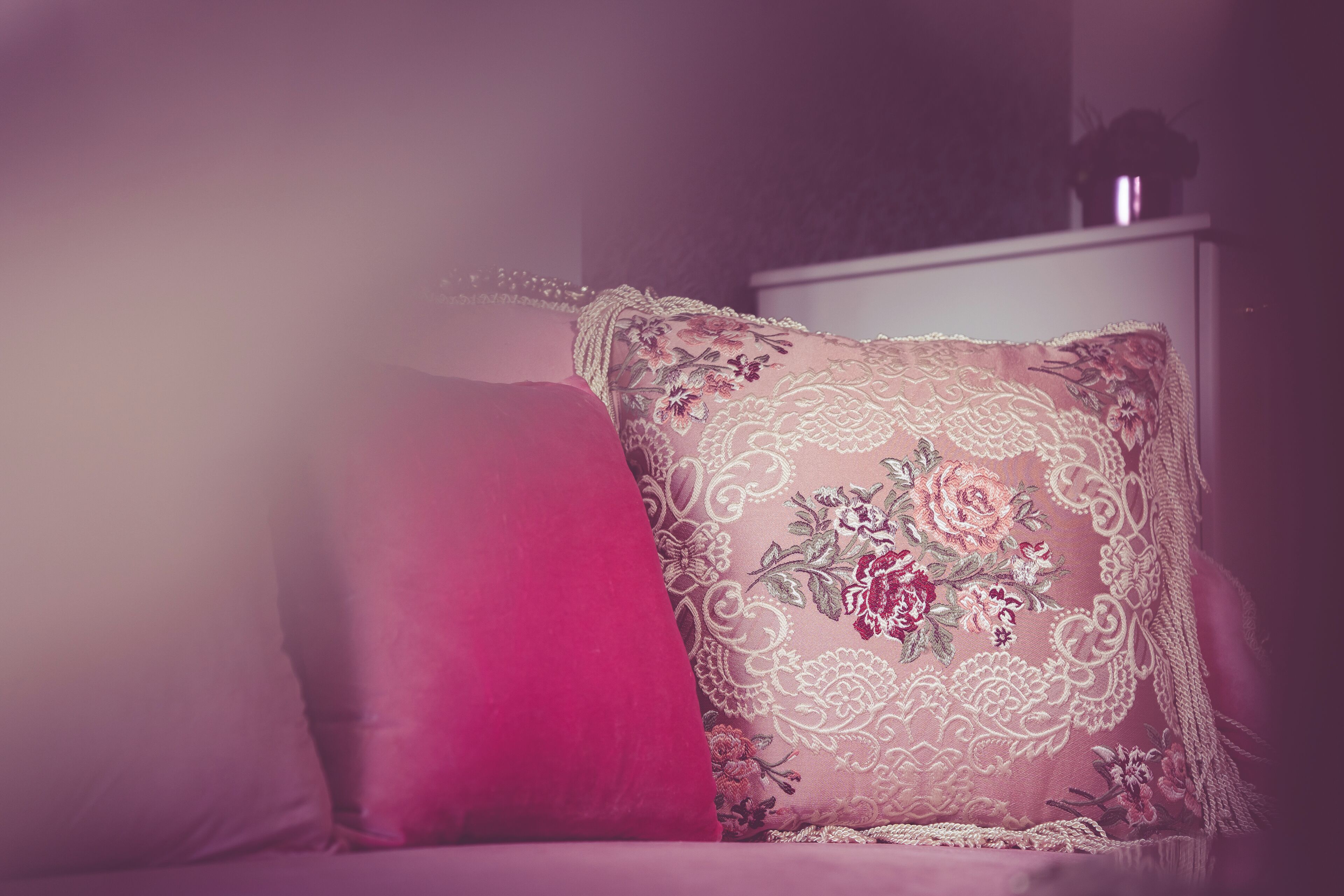 Una cama con un almohadón rosa y un cojín decorado con bordados florales.