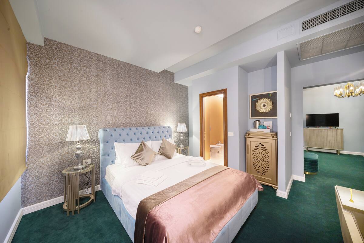 Une chambre d’hôtel avec un grand lit, une coiffeuse avec un miroir, une télévision et un lustre.