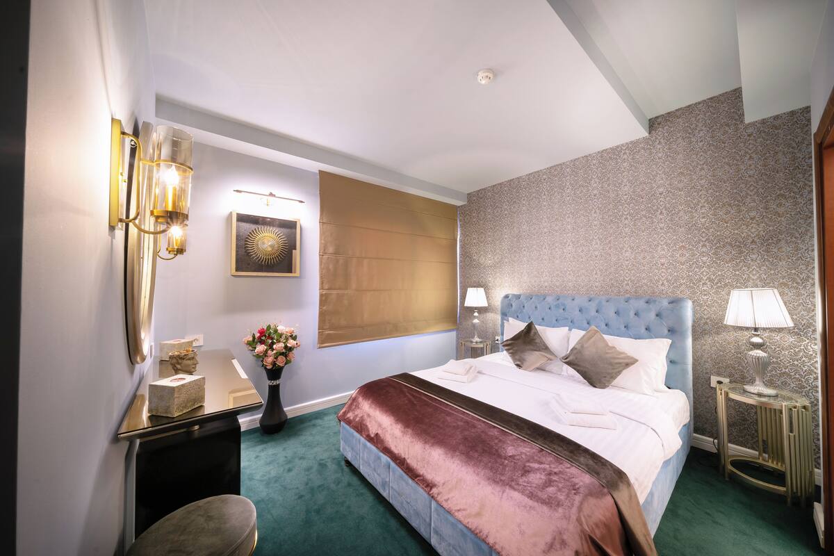 Une chambre d’hôtel comprenant un lit, des tables de chevet, un bureau, une chaise, un vase avec des fleurs et une œuvre d’art accrochée au mur.