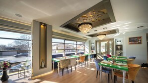 Een modern restaurant met houten vloeren, groen en wit aangerichte tafels, en een kroonluchter.