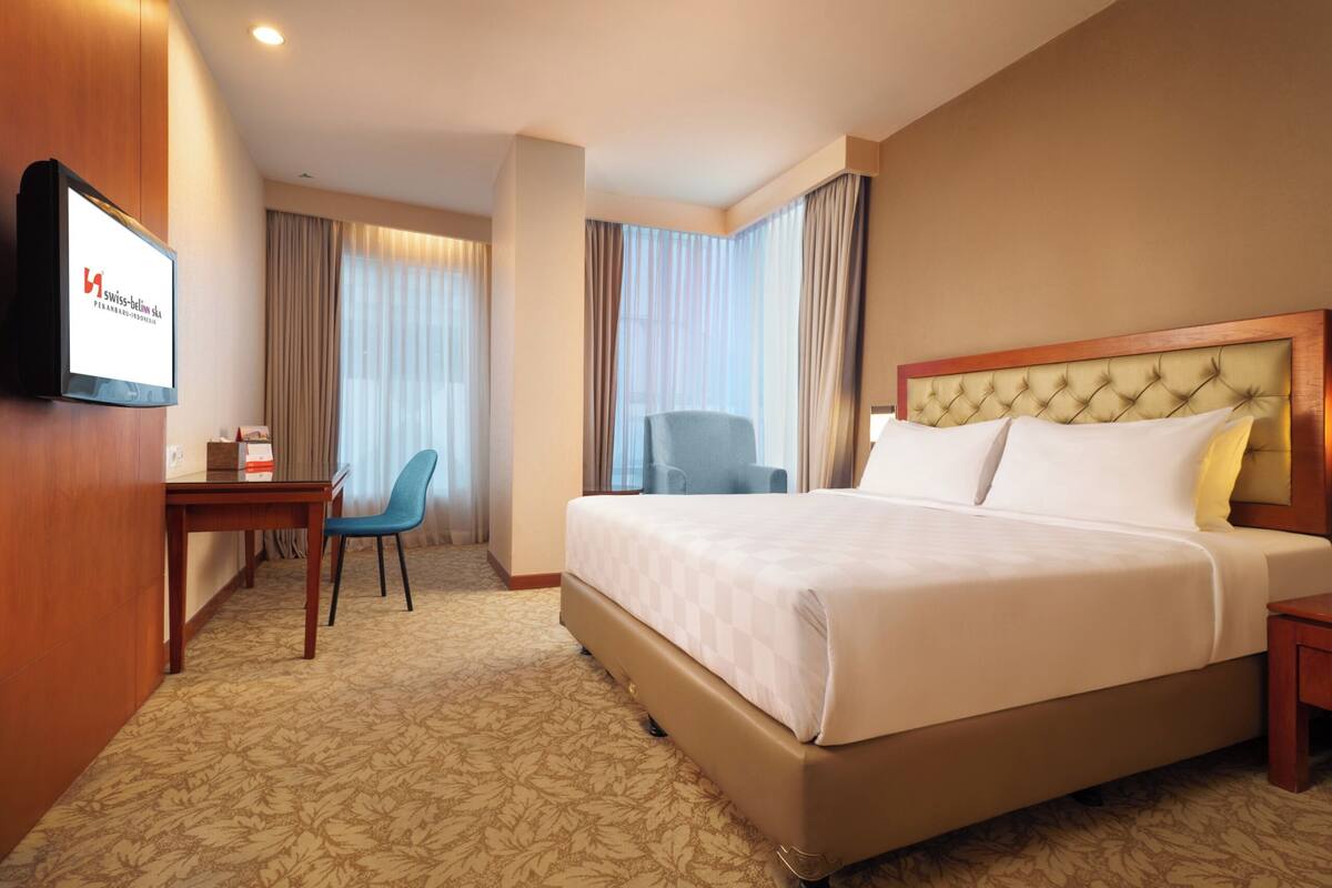 A hotel room with a large bed, a desk, a chair, and a television on the wall.
