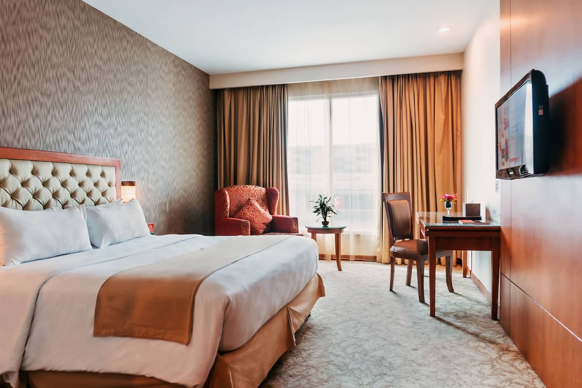 A hotel room with a large bed, a desk, a chair, a television, and a window with curtains.