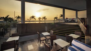 An outdoor seating area with tables and chairs, overlooking a sunset view with palm trees. - Swiss Belinn SKA Pekanbaru (Pekanbaru)