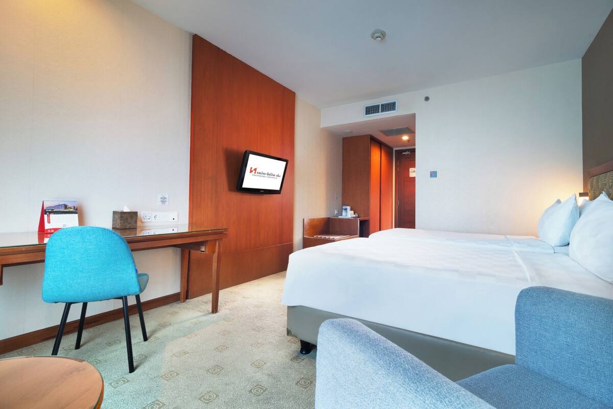 A hotel room with a bed, a desk, a chair, and a television.