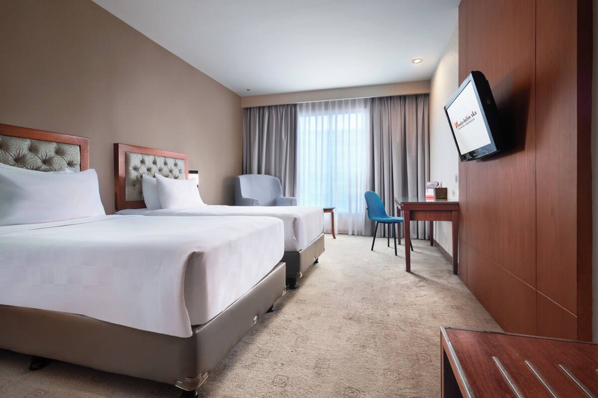 A hotel room with two beds, a desk, a chair, and a television on the wall.