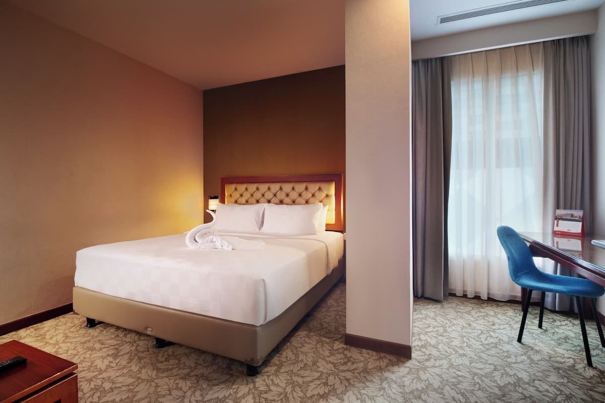 A hotel room with a large bed, a desk with a chair, and a window with curtains.
