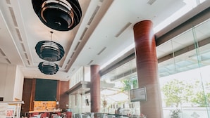 A spacious indoor area with multiple seating arrangements, including tables and chairs, and a large window providing natural light. - Swiss Belinn SKA Pekanbaru (Pekanbaru)