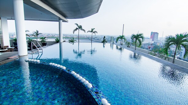 A modern infinity pool with clear blue water, surrounded by palm trees and a cityscape view. - Swiss Belinn SKA Pekanbaru (Pekanbaru)