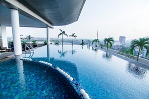 A modern infinity pool with clear blue water, surrounded by palm trees and a cityscape view.