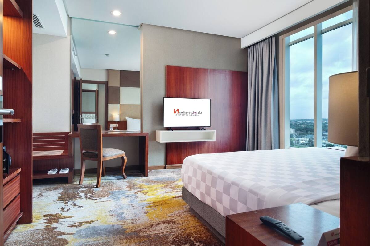 A hotel room with a bed, a desk, a TV, and a view of the city.
