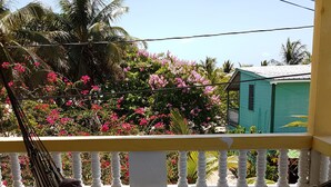 A person relaxing in a hammock on a balcony with a view of pink flowers and a green building in the background. - Serenade Hotel (Placencia)